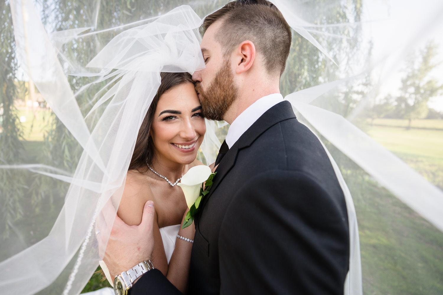 Intimate close-up of the groom kissing the bride’s forehead under her veil.