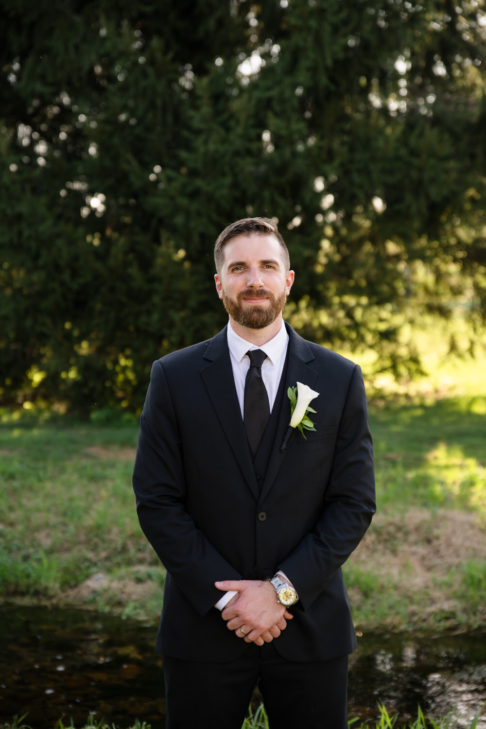 Groom in a classic black suit and tie posing in a field during golden hour.