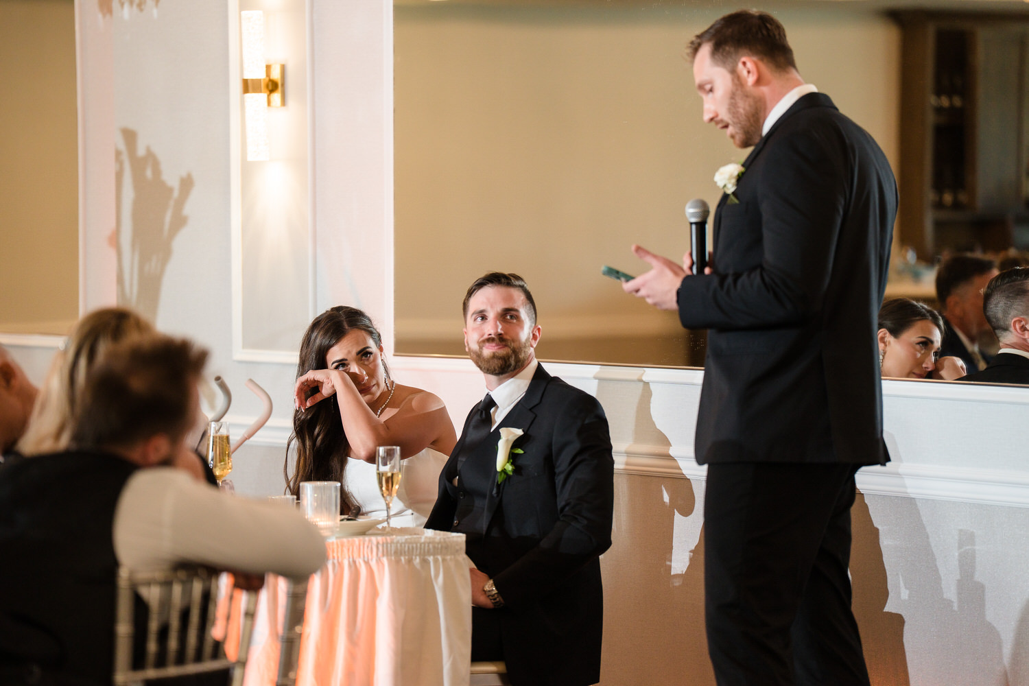 Candid of the bride and groom listening to a wedding toast at their sweetheart table.
