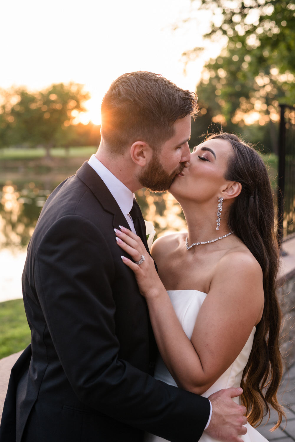 Stunning sunset wedding portrait of the couple kissing by the lake.