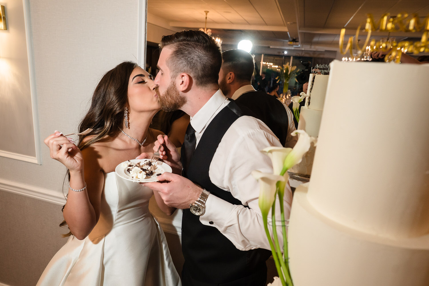 Bride and groom sharing a romantic kiss while cutting their wedding cake.