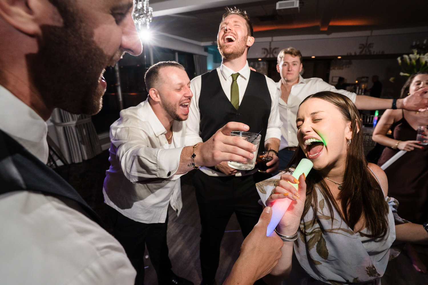 Wedding guests laughing and holding drinks while dancing at the reception.