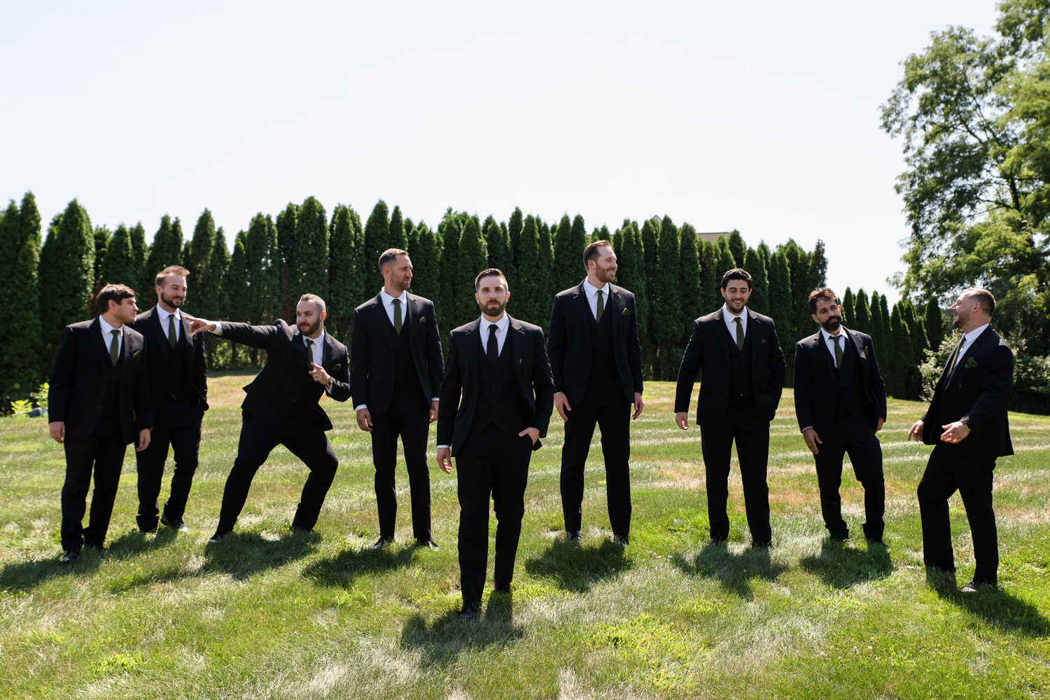 Groomsmen posing together in a line on the golf course during a sunny day.