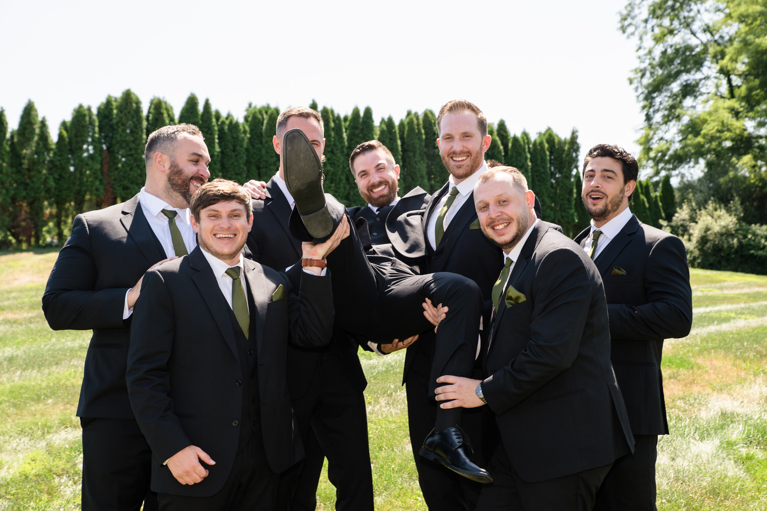 Groomsmen in black suits lifting the groom up for a fun group photo.