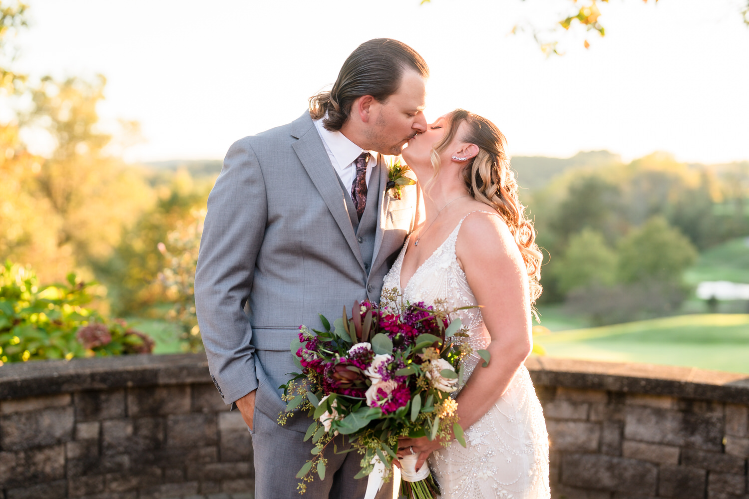 Romantic Golden Hour portrait of a bride and groom kissing on the Woodstone golf course with soft sunlight flares.