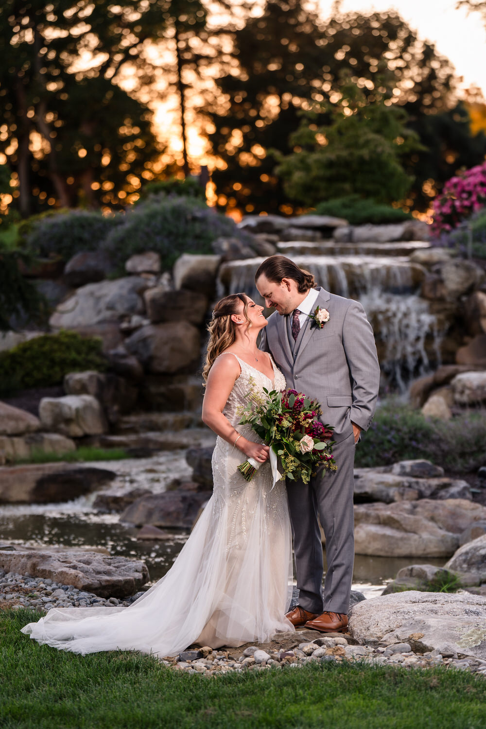 Candid kiss between a bride and groom in front of the scenic waterfall at Woodstone Country Club.