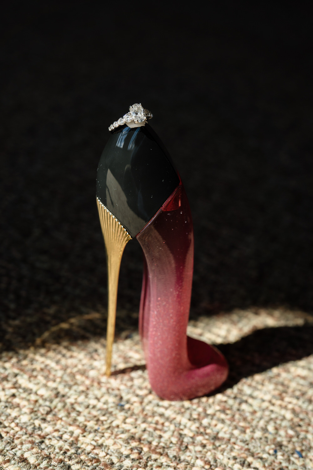 High-contrast "bold edge" portrait of a Carolina Herrera Good Girl perfume bottle and the wedding ring.