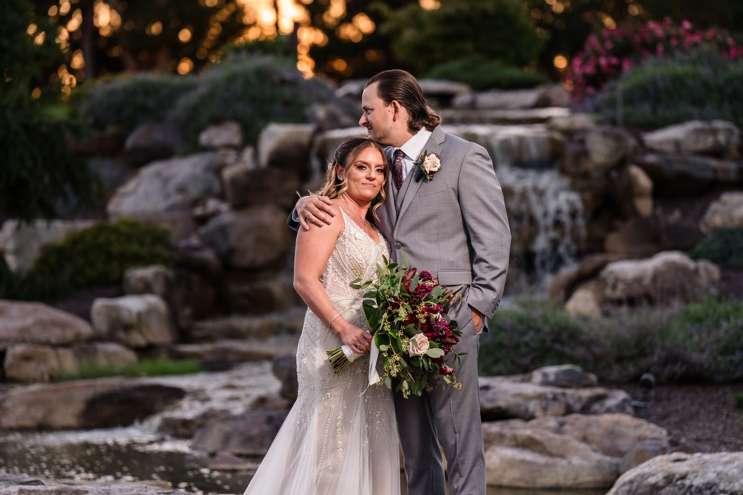 Full-length wedding party portrait in the Woodstone Gardens featuring burgundy bridesmaids' dresses and grey suits.