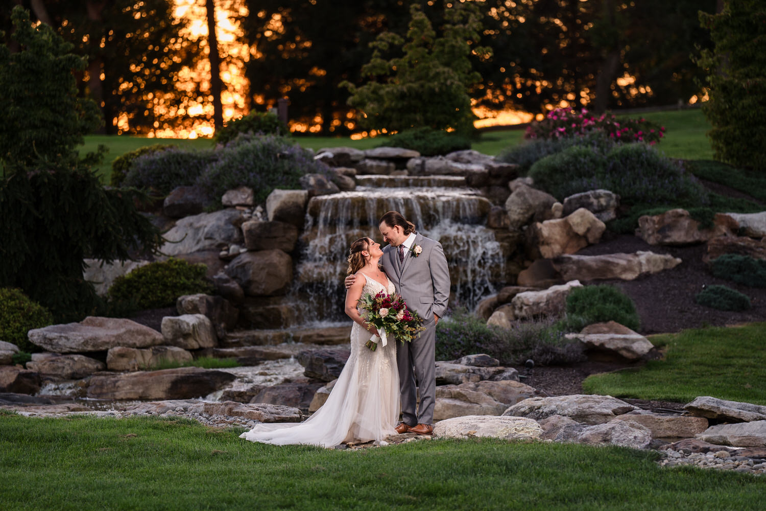 True-to-life portrait of a bride and groom posing in front of the stone waterfall at the Woodstone Gardens.