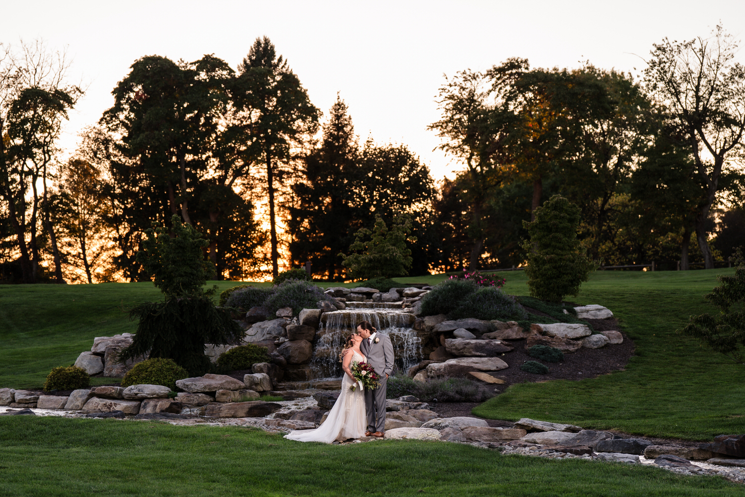 Wide-angle landscape of the Woodstone Country Club ceremony site featuring the waterfall and Blue Mountain horizon.