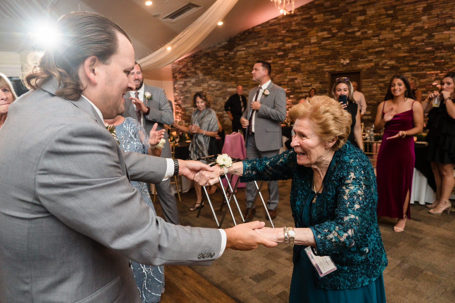Heartfelt candid of a groom dancing with an elderly family member on the Woodstone Grand Ballroom dance floor.