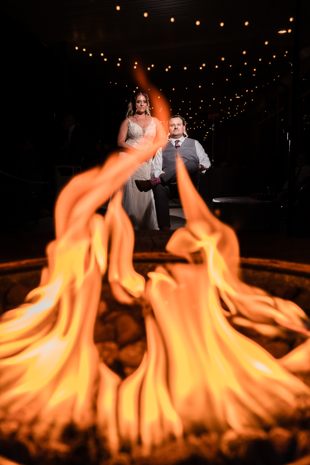Creative night portrait of a bride and groom framed by the warm, dramatic glow of an outdoor fire pit at Woodstone.
