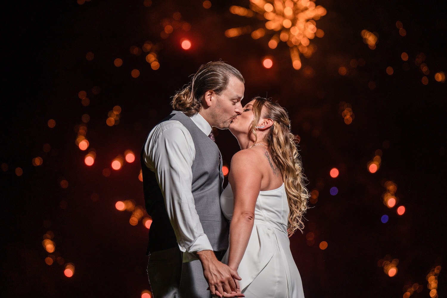 Intimate night portrait of a bride and groom silhouetted against a vibrant, bokeh-filled background of reception lights.
