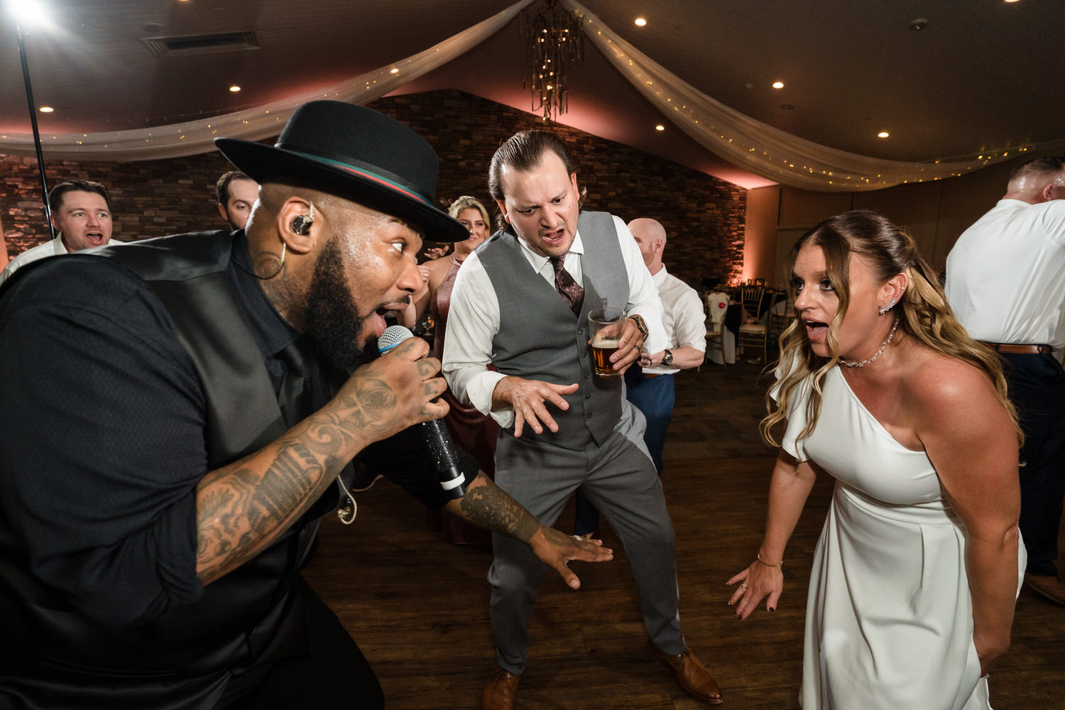 High-energy reception candid of the groom singing into a microphone on the Woodstone Country Club dance floor.