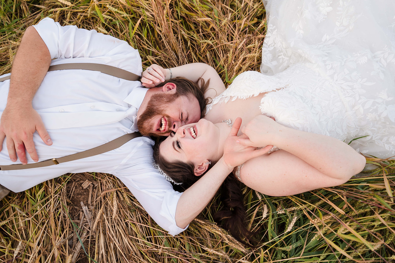 Bride and Groom laying on the ground laughing in a cornfield