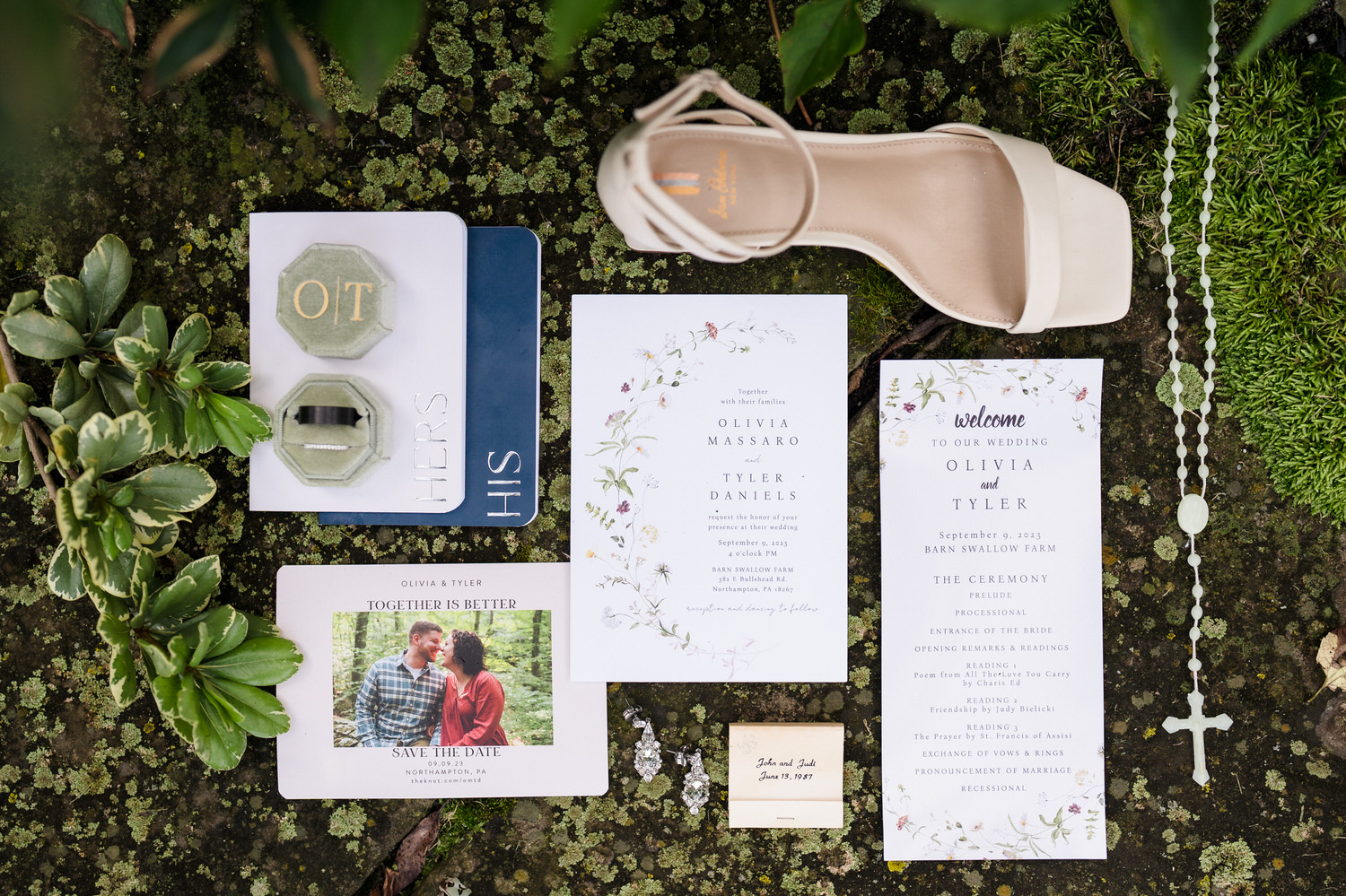 Flat lay of a floral wedding invitation suite with rings and a tan envelope.