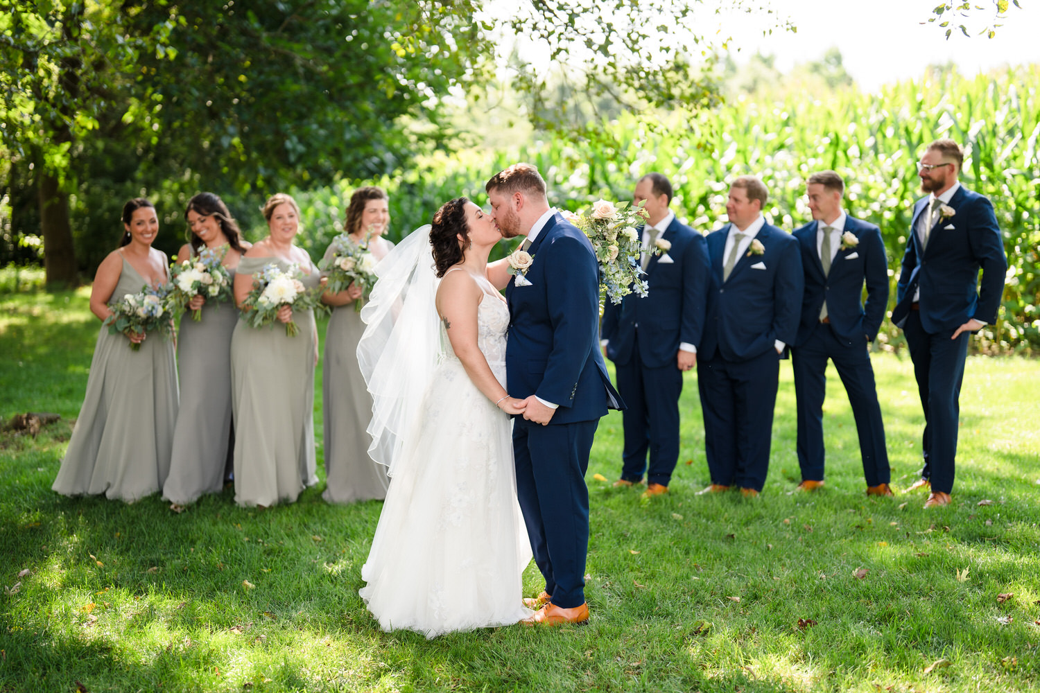 Romantic portrait of the bride and groom sharing a kiss in a sun-drenched field in front of their wedding party