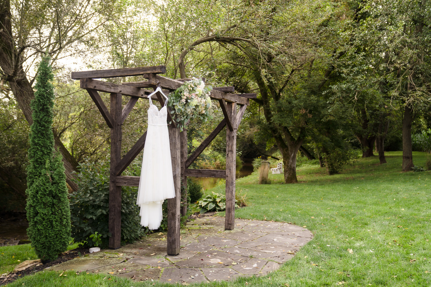 Simple and elegant outdoor ceremony altar featuring a wooden arch and white gown.
