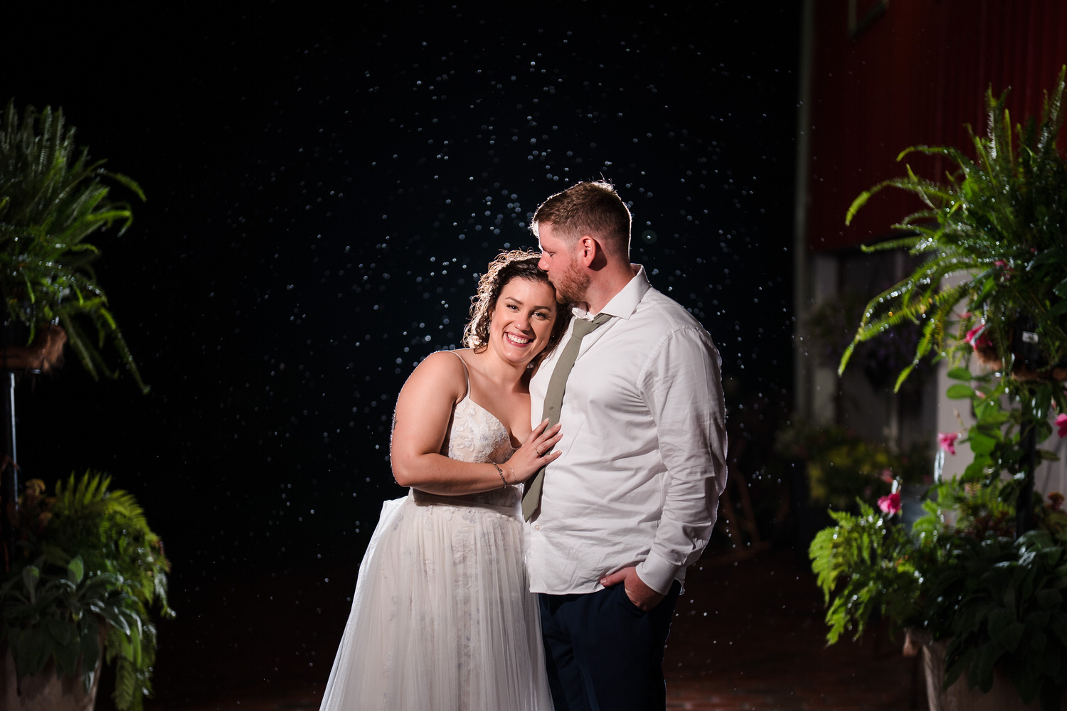Wide backlit night shot of the couple standing together in the rain.