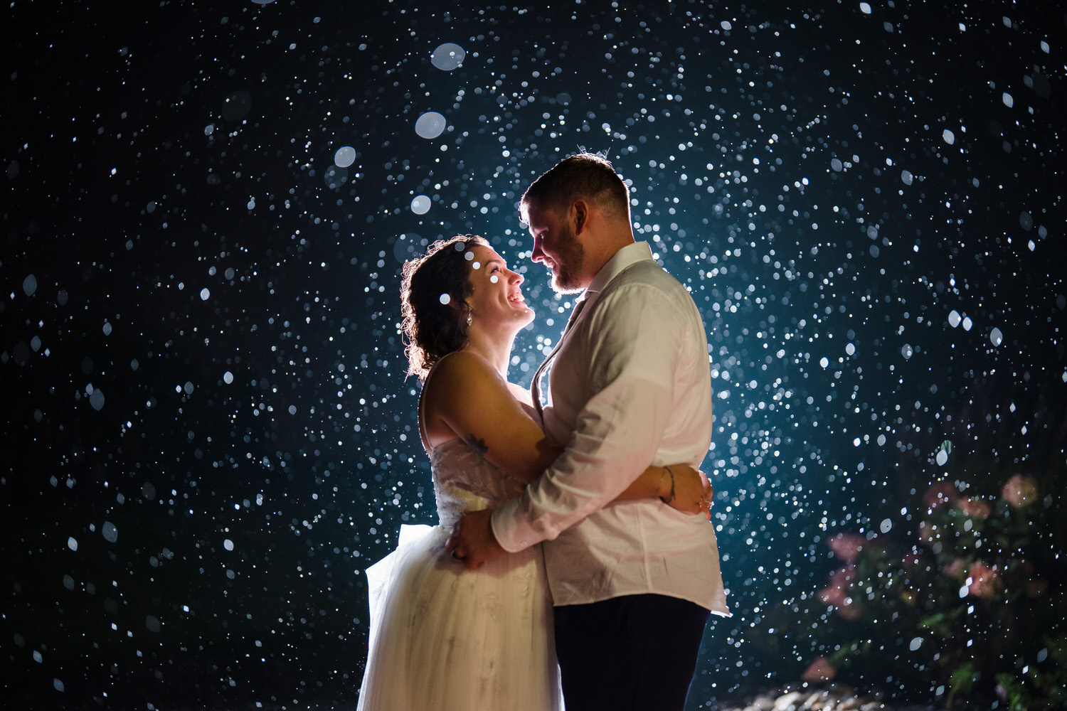 Creative night shot of the bride and groom embracing under falling rain.