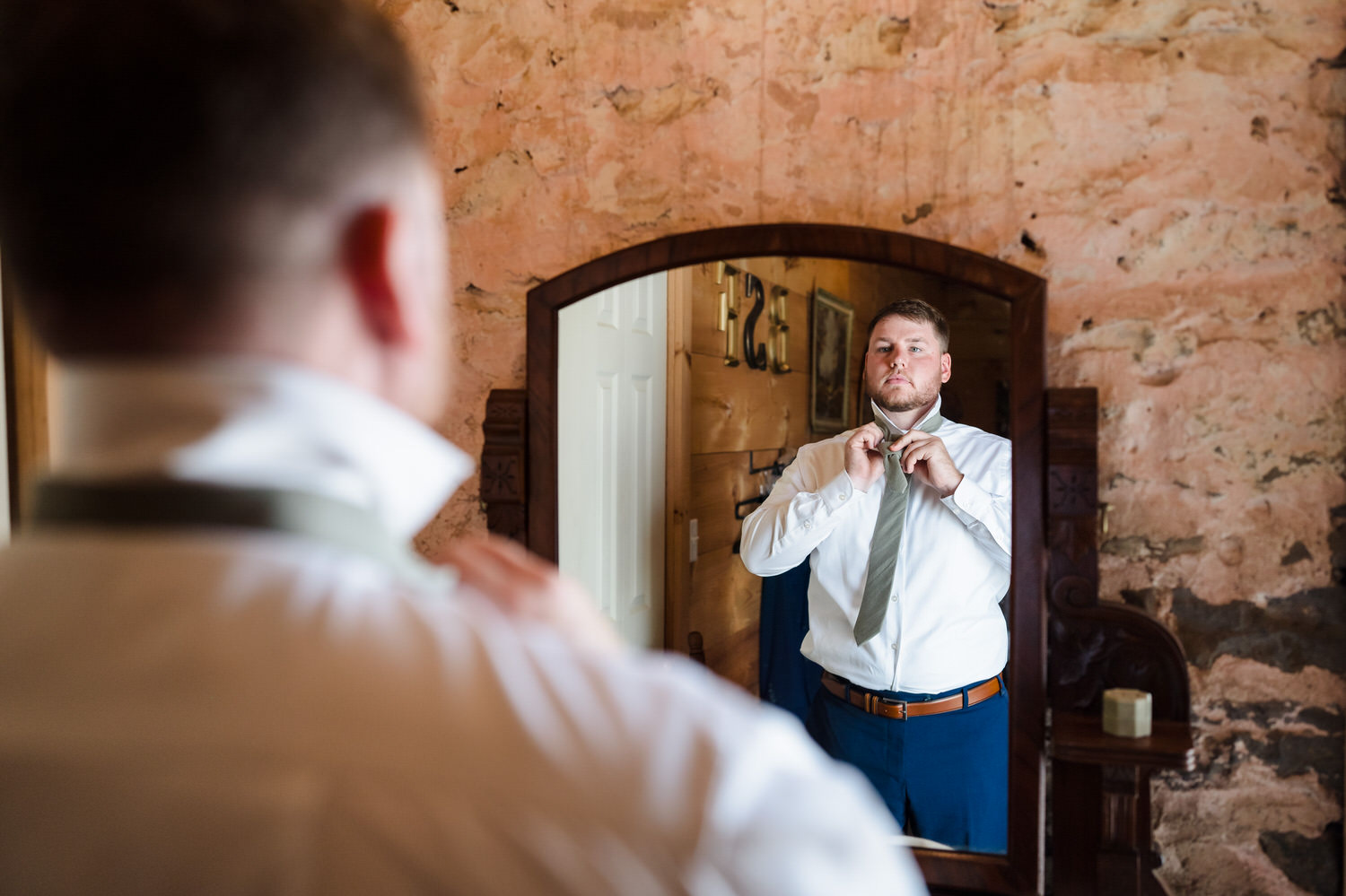 Groom adjusting his tie in a mirror while getting ready for the wedding.