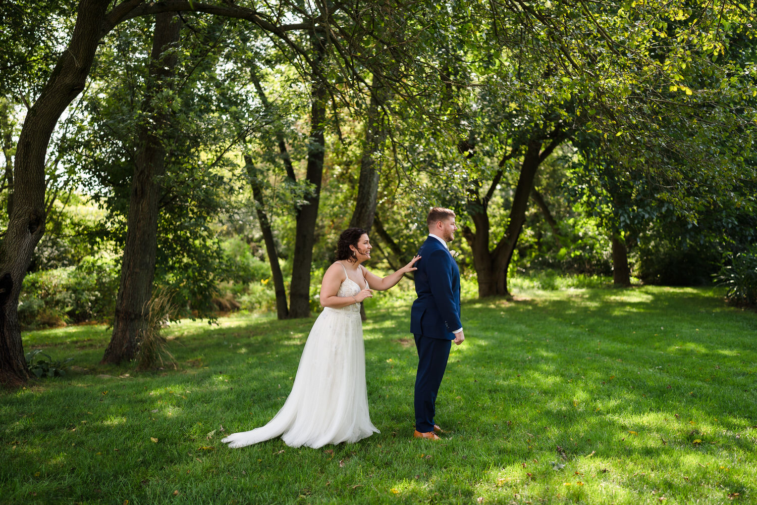 Wide shot of a first look moment between the couple in a green field.