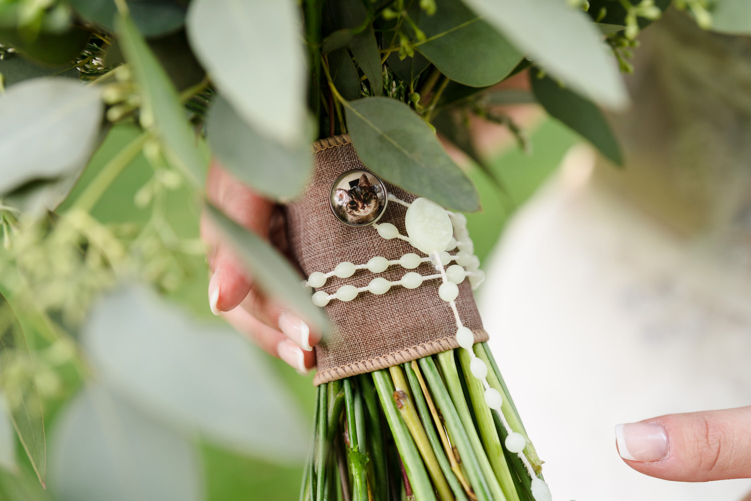 Detail shot of a wedding bouquet wrap featuring a rustic burlap and lace design and a charm of Olivia's cat.