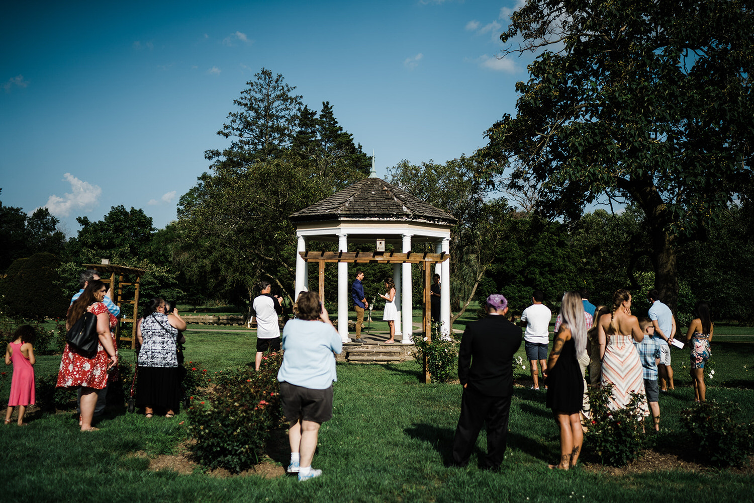 Small outdoor wedding ceremony at a white gazebo surrounded by lush greenery at Allentown Rose Gardens in PA.