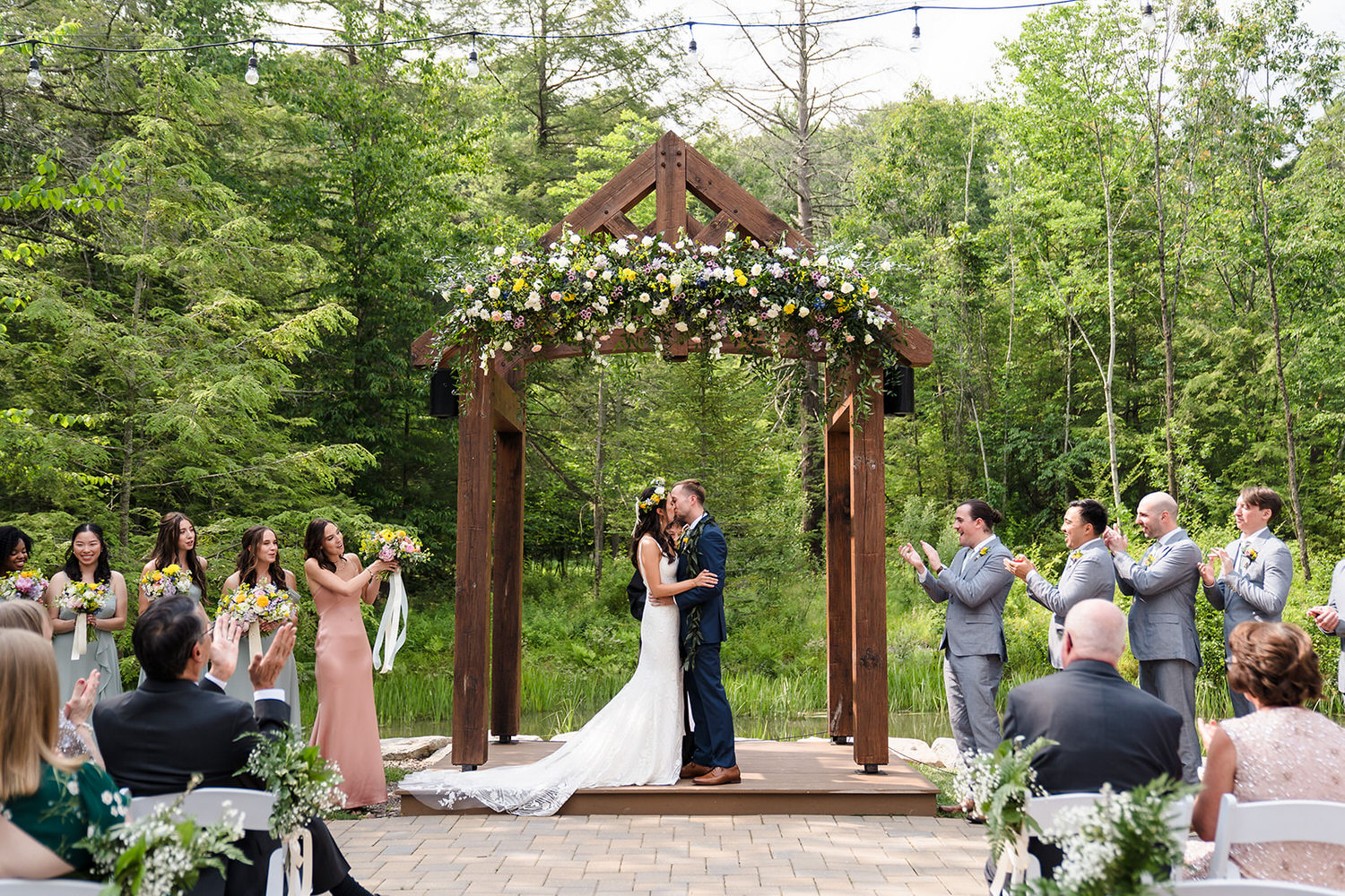 Newlyweds kissing under a timber-frame lakeside arch at Catalpa Grove in Bucks County.