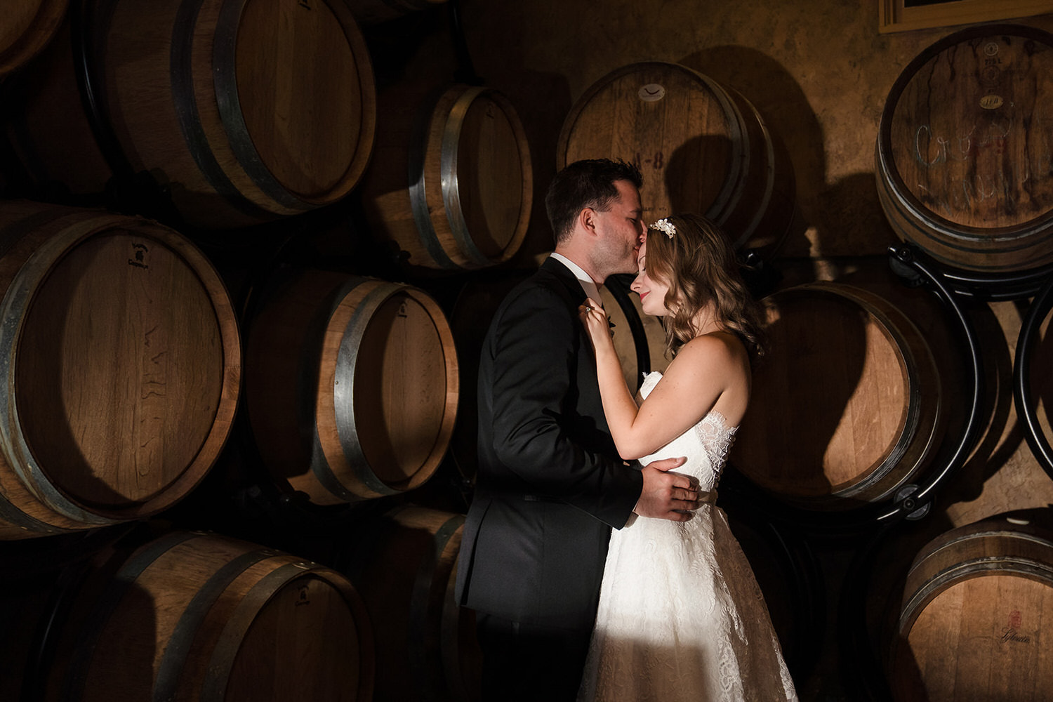 Groom kissing bride's forehead in a dimly lit wine barrel room at Crossing Vineyards & Winery in Bucks County.