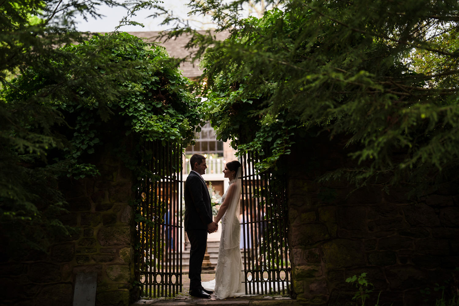 Newlyweds holding hands between ivy-covered stone walls in the gardens at Holly Hedge Estate in Bucks County.