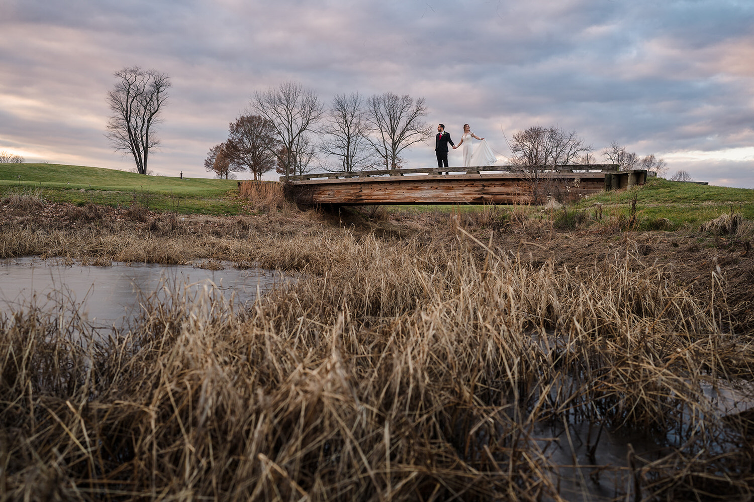Bride and groom standing on a wooden bridge overlooking the marsh and golf course at Riverview Country Club in Easton, PA.