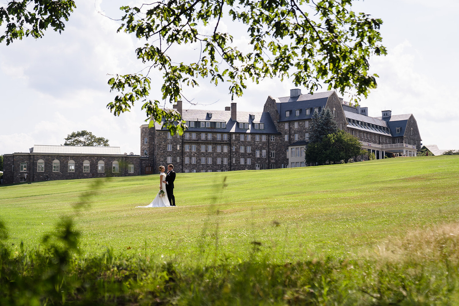 Wedding couple posing in a wide field in front of the grand historic Skytop Lodge resort in the Poconos.
