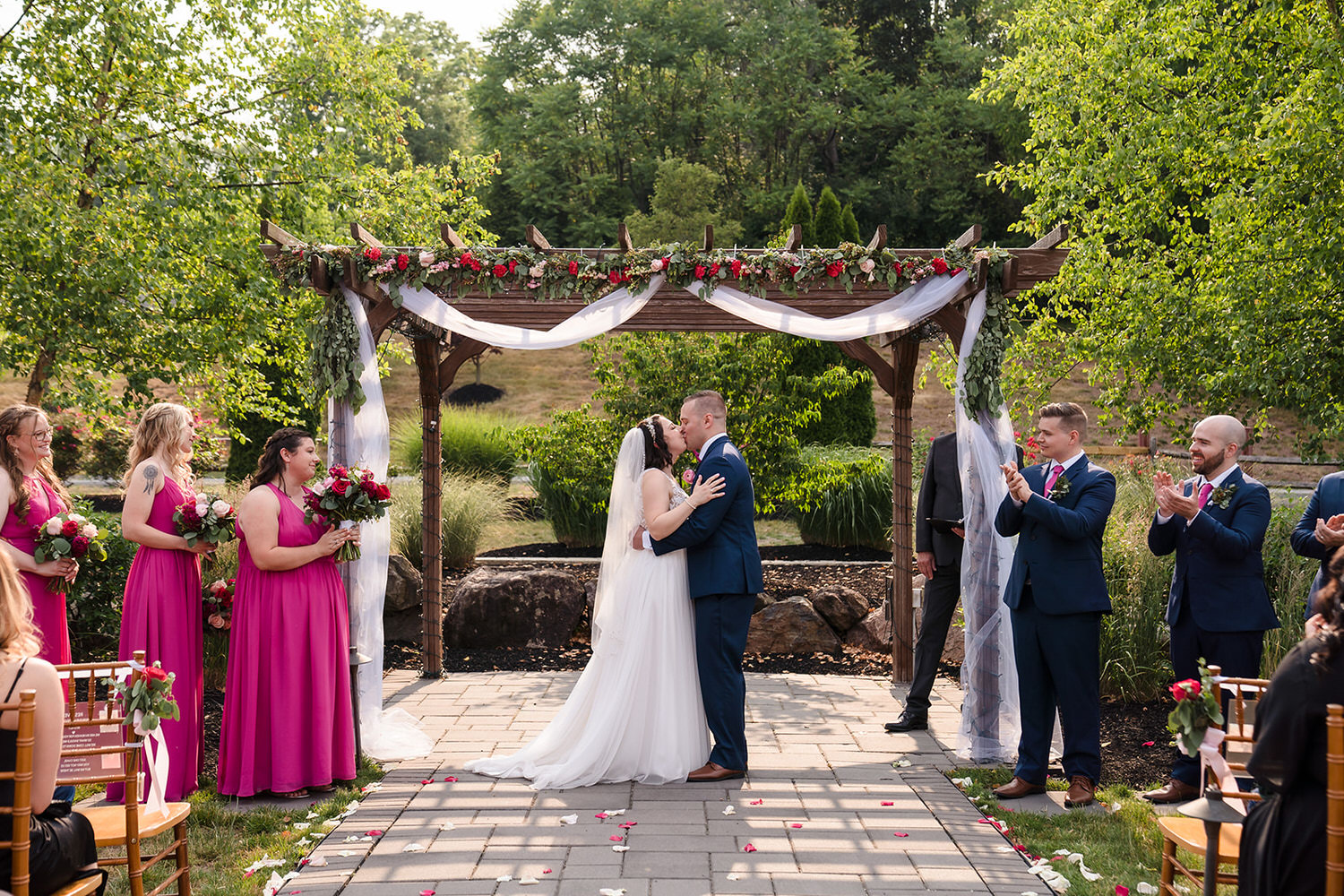 Newlyweds kissing under a rustic wooden pergola during an outdoor ceremony at Sunnybrook Ballroom in Montgomery County.