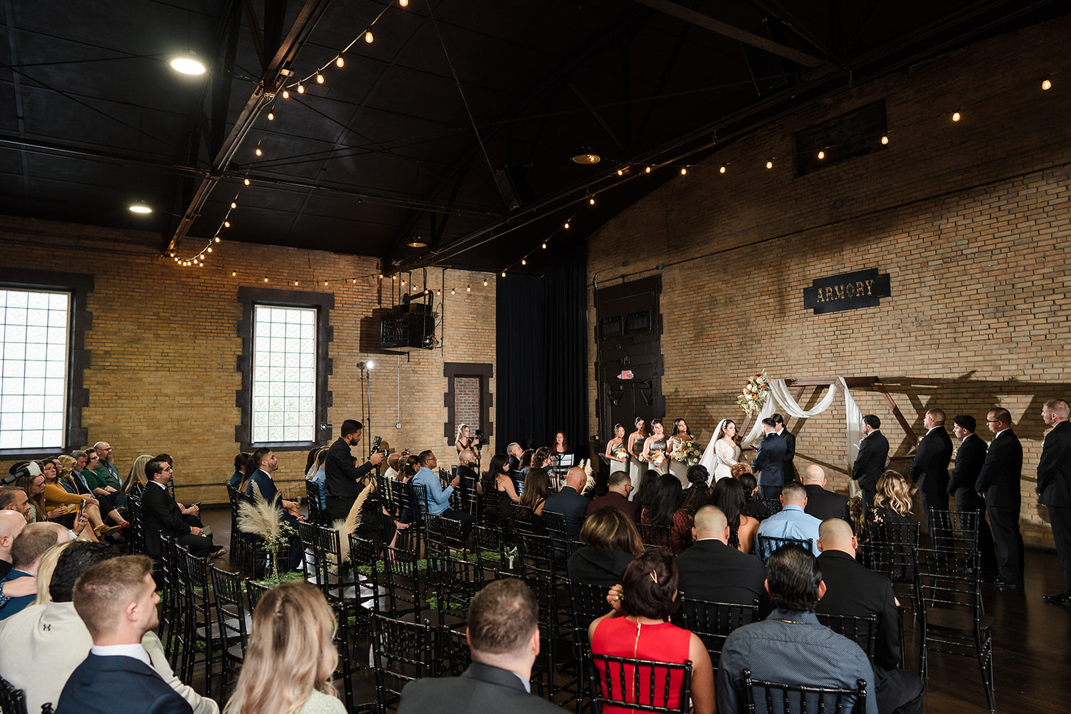 Indoor wedding ceremony with string lights and exposed brick in the historic industrial space at The Armory Events near the Lehigh Valley.