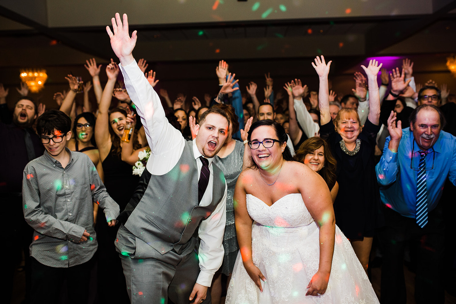 Newlyweds posing for a group photo with a large group of guests on the dance floor in the ballroom at The Palace Center in Allentown, PA.