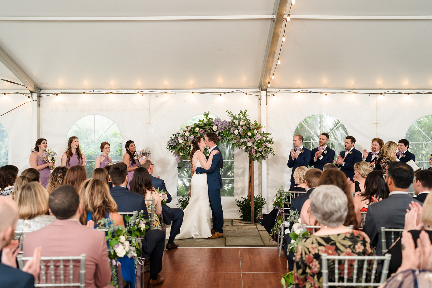 Bride and groom sharing a first kiss under a tented terrace with elegant floral decor at The Sayre Mansion in Bethlehem, PA.