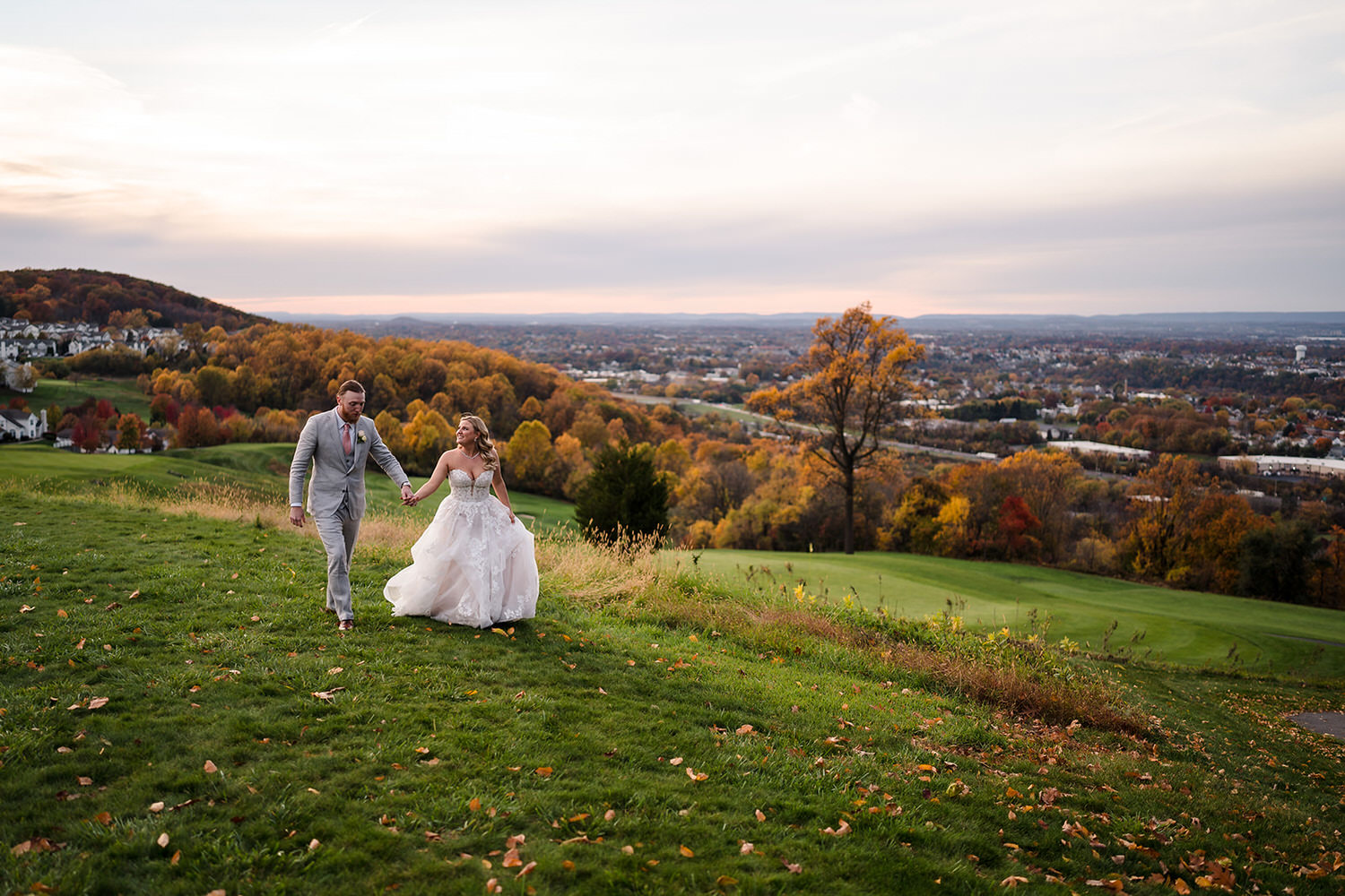Bride and groom walking through high grass with panoramic vistas of the Delaware River Valley at The View at Morgan Hill in Easton, PA.