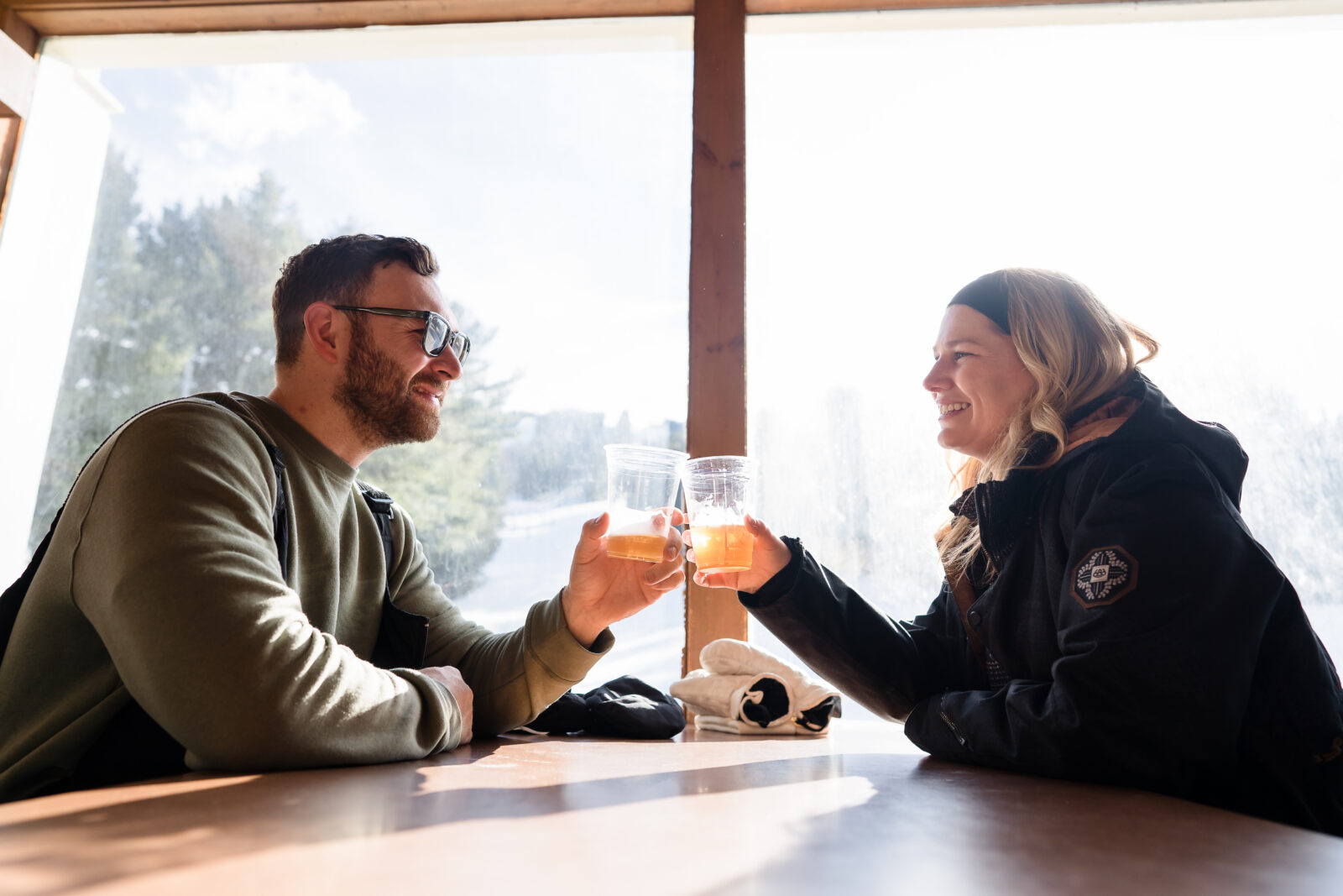 Couple toasting drinks inside ski lodge during cozy winter engagement session