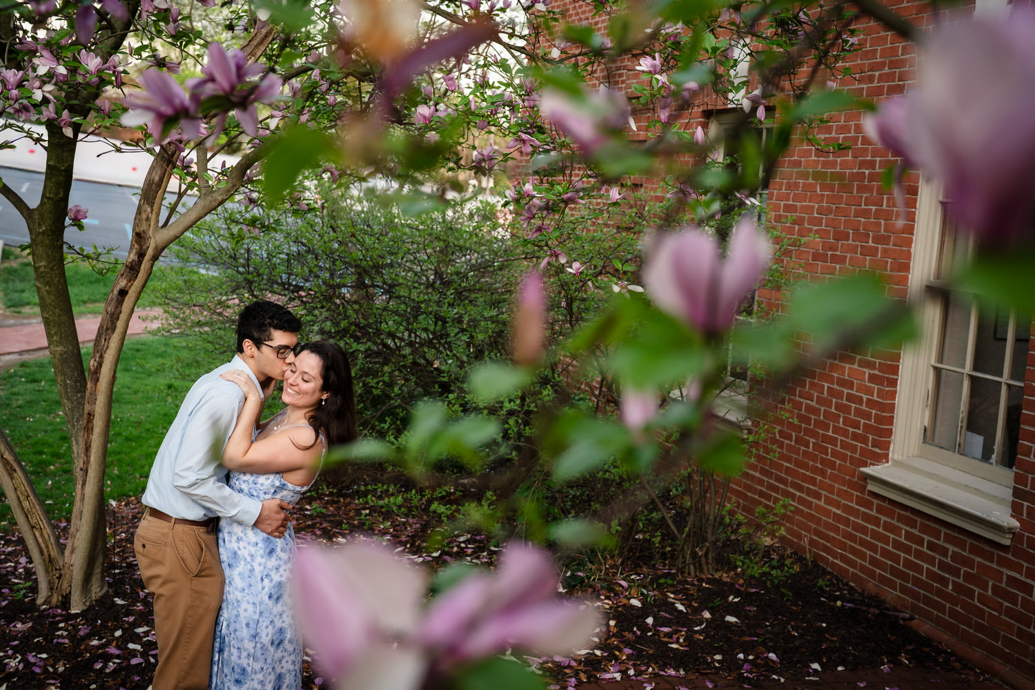Couple kisses framed through pink magnolia blossoms in the foreground

