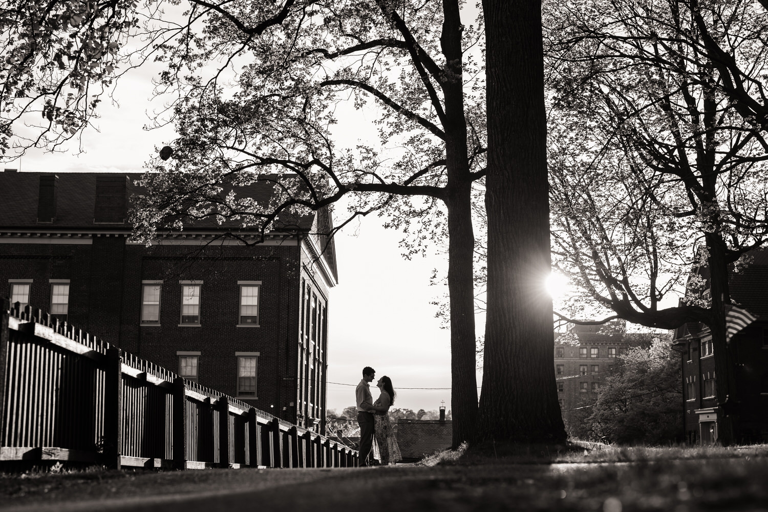 Distant black and white silhouette of a couple looking at one another framed by trees with sunset glow behind, Moravian University, Bethlehem PA
