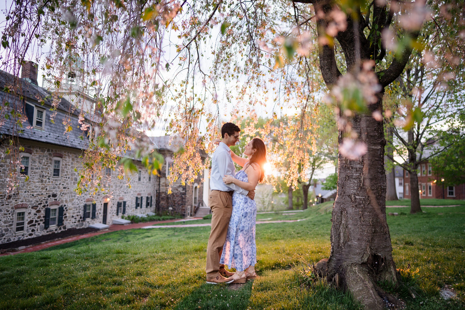 Bride-to-be smiles in fiancé's arms at sunset on the Moravian campus