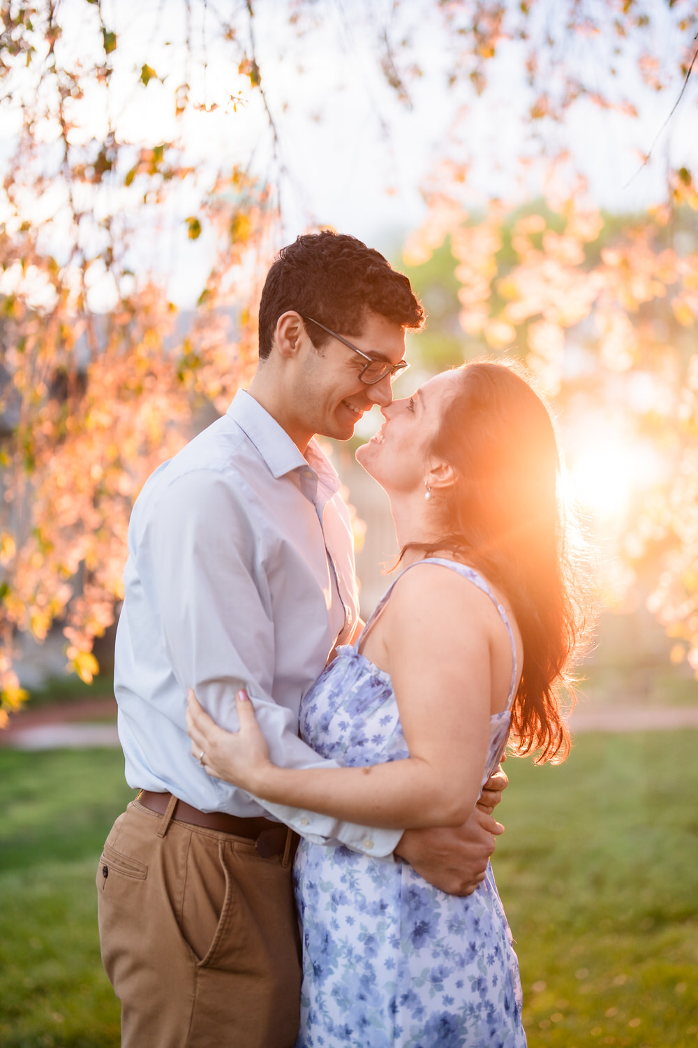 Couple laughs together with golden hour sunburst breaking through the leaves
