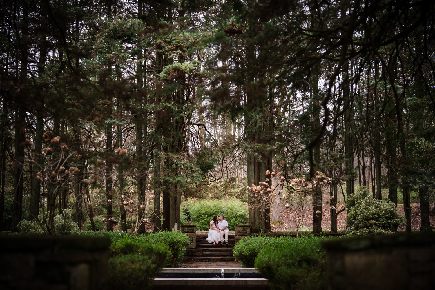Couple sitting along manicured garden path with trees and hedges