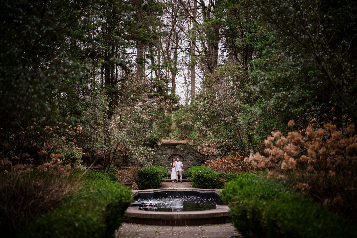 Symmetrical garden fountain with couple in distance during engagement shoot