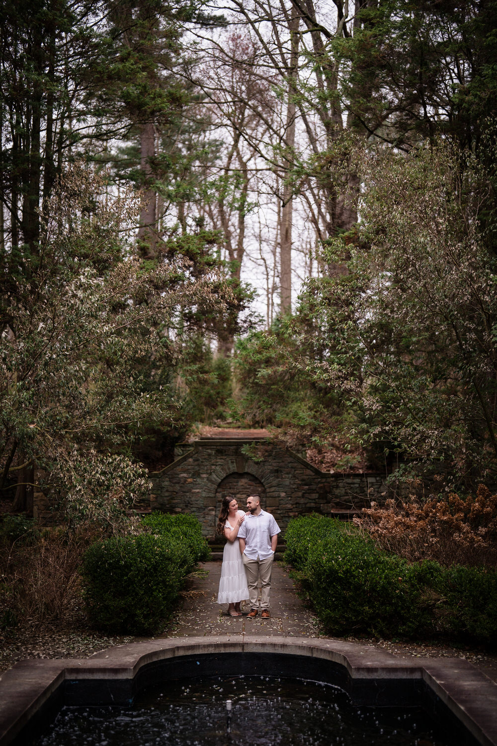 Couple walking through wooded garden path during engagement session