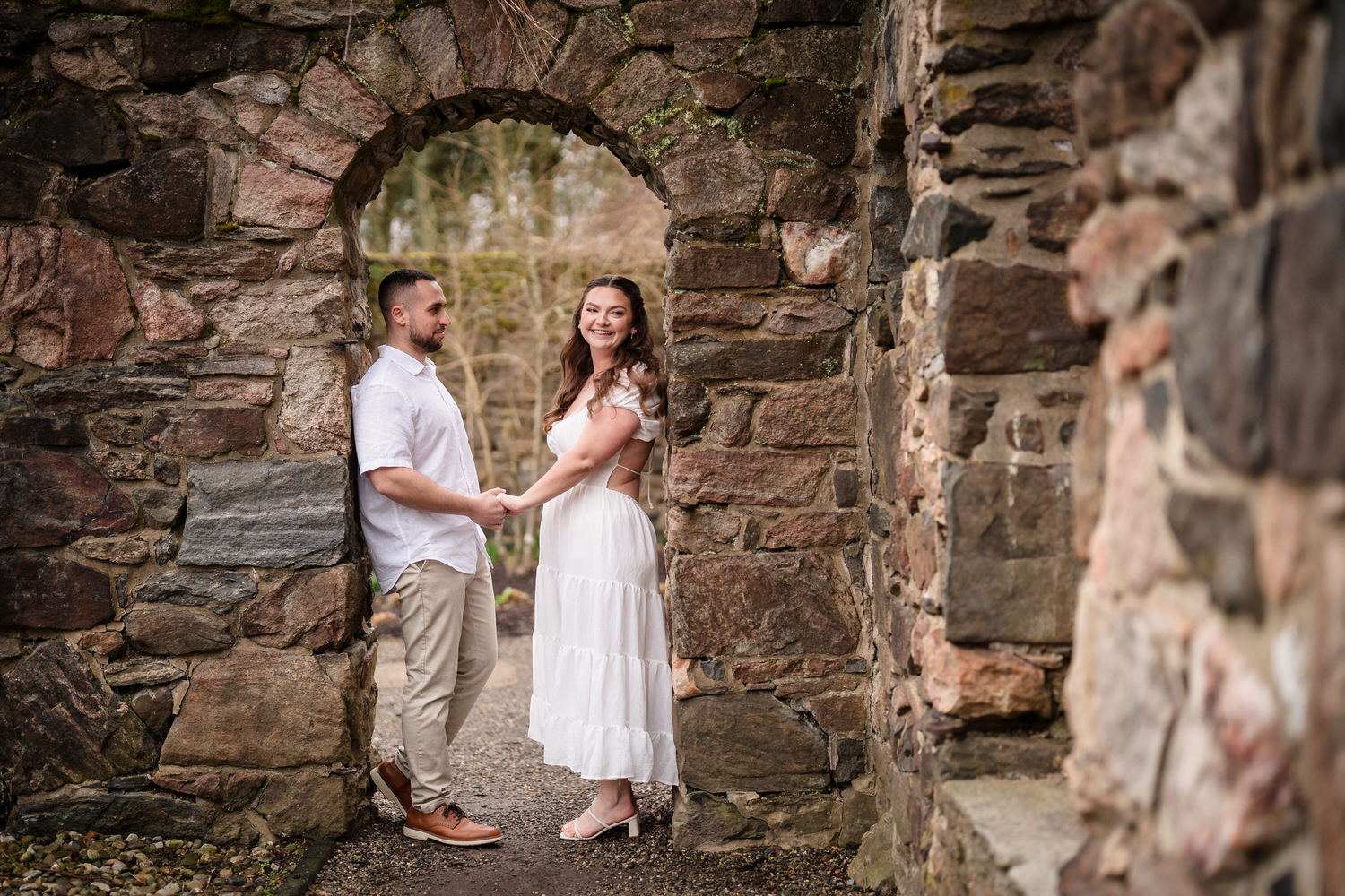 Couple holding hands under historic stone arch during engagement shoot