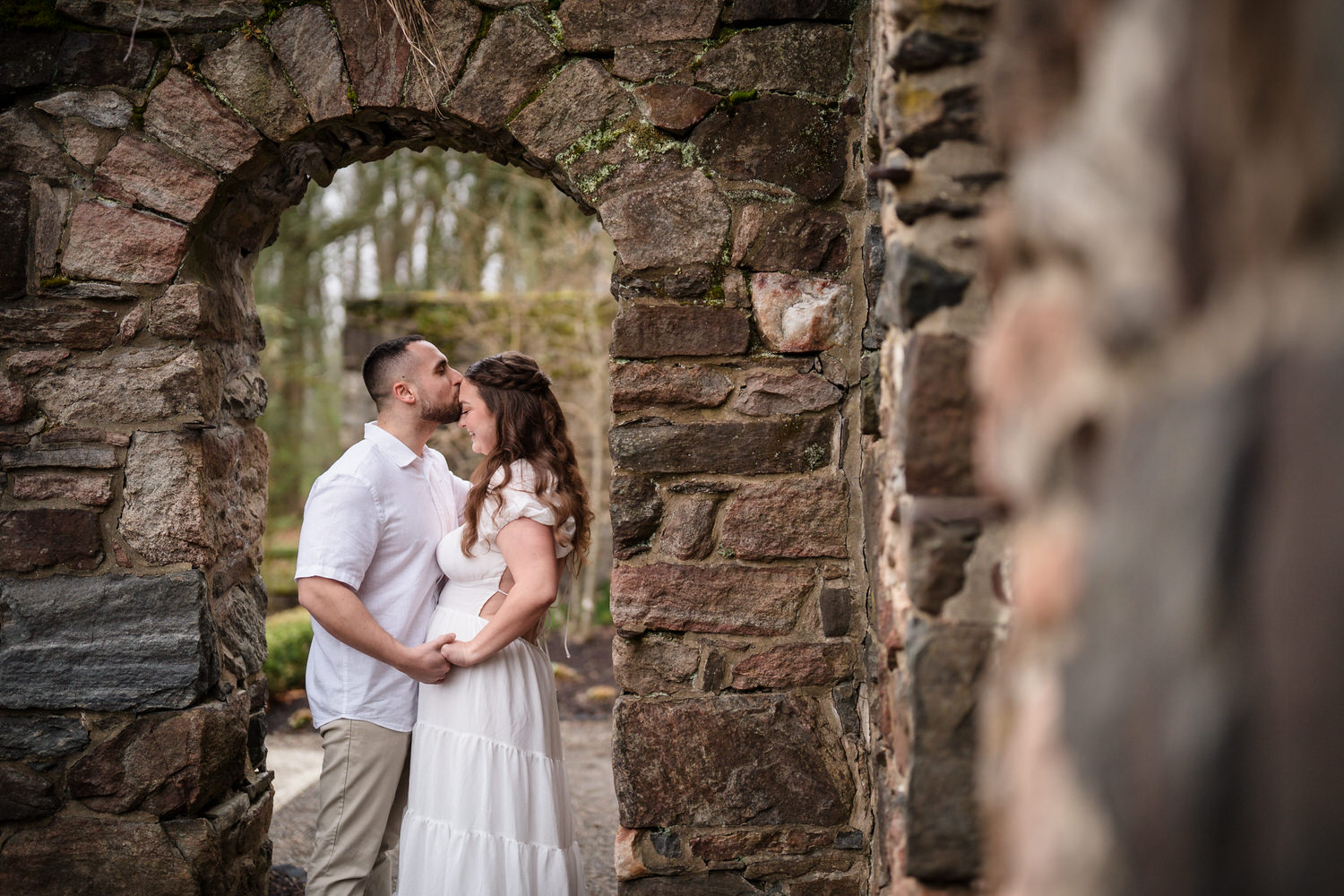 Romantic engagement pose of couple under stone arch ruins