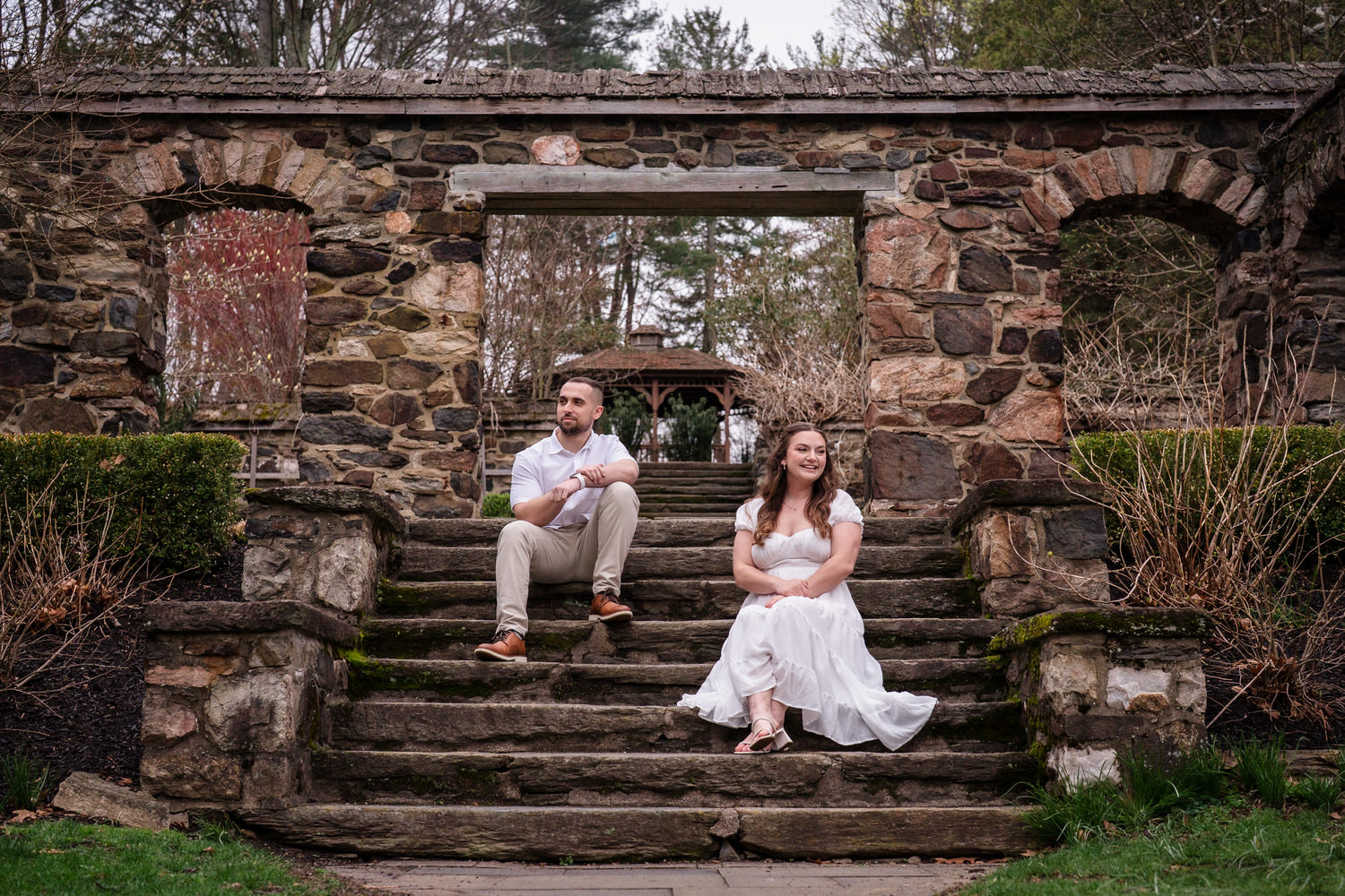 Playful engagement photo of couple sitting on stone steps in garden ruins
