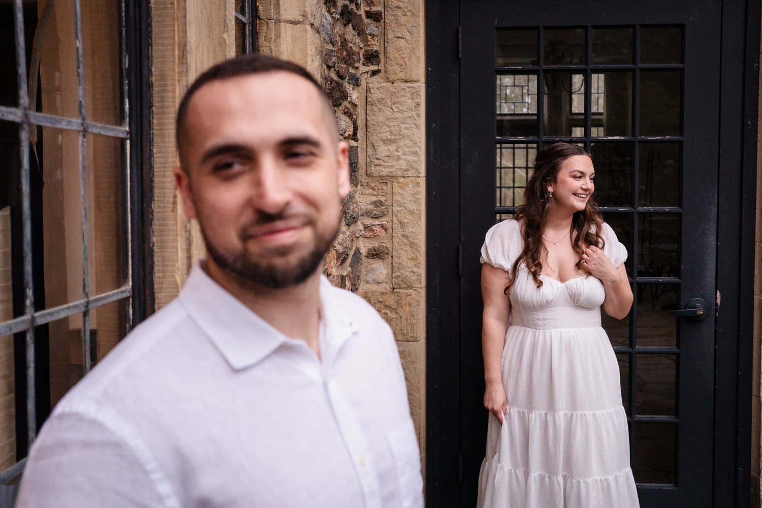 Groom portrait close-up with bride blurred in background at stone venue